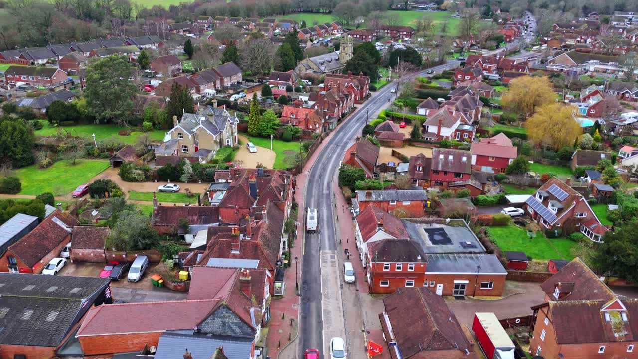 Lotnicze panoramiczne ujęcie z drona nad podmiejskim Southampton, przedstawiające zabudowę wioski Botley o zachodzie słońca w pochmurny, zimowy dzień, z samochodami przejeżdżającymi po drogach poniżej, mijającymi małe domy w miasteczku.