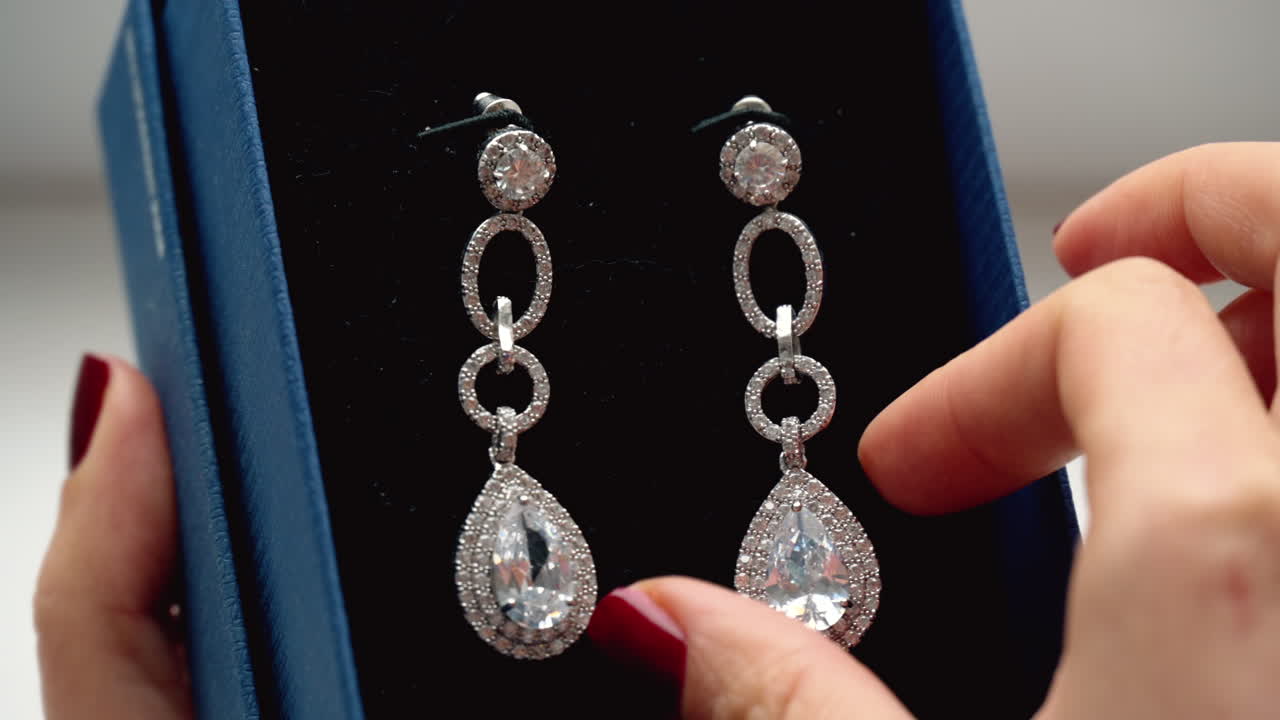 Woman hands playing with pear cubic zirconia drop earrings in a blue box