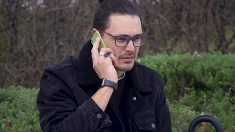 un hombre serio con una chaqueta negra y gafas tiene una llamada telefónica tensa