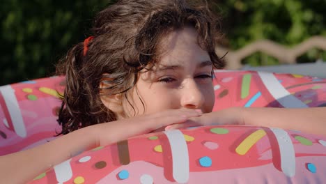 11-12 años feliz chica caucásica linda acostada en un círculo de rosquilla inflable en la piscina en un jardín. vacaciones de verano frescas para niños y niños. juegos en el agua. donat rosa. 4k cámara lenta