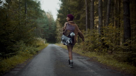 woman with backpack walking on road by forest