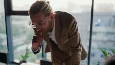 close-up shot of a blond man in glasses with a beard in a light suit leans his hands on the table and tells his colleagues what needs to be done in a modern office