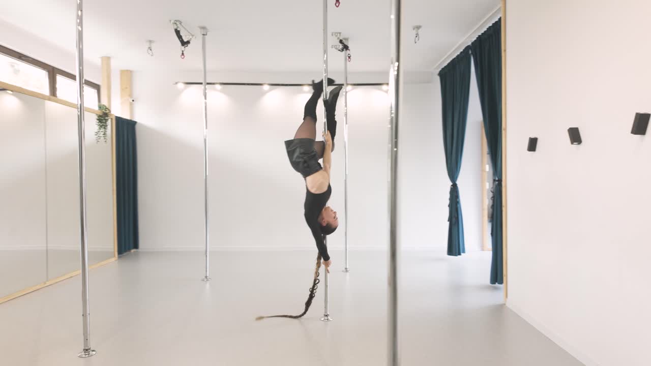 Strong athletic dancer doing acrobatics in pole dance bar
