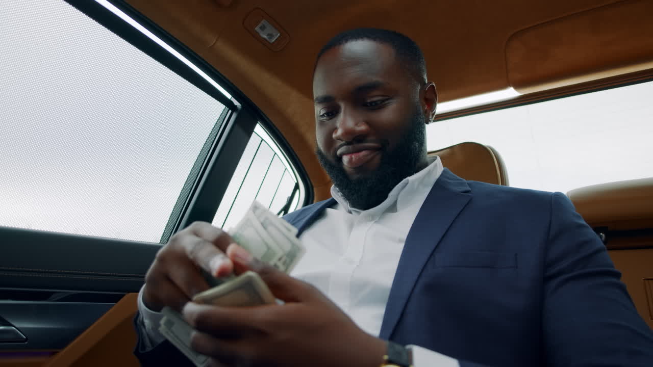African man smelling dollars at car