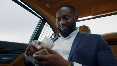 african man smelling dollars at car