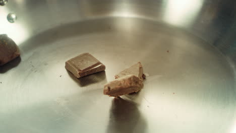 closeup chunks of chocolate falling into metal pan in slow motion.