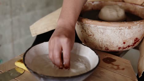 Female-artist-potter-in-the-workshop-creating-a-ceramic-product.-Woman-splashing-water-on-a-clay-piece-on-spinning-wheel.-Creative-workshop.-Slow-motion