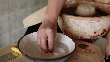 female artist potter in the workshop creating a ceramic product. woman splashing water on a clay piece on spinning wheel. creative workshop. slow motion