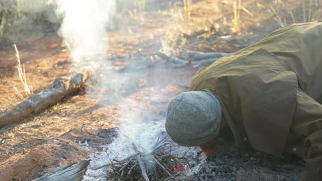 a bushman blows on a campfire to get it started in the australian outback