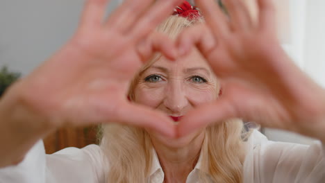 senior grandmother woman makes symbol of love showing heart sign to camera express romantic feelings