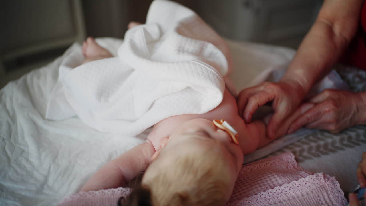 Baby lying on their back while an adult massages them and the mother holds the pacifier in the baby's mouth