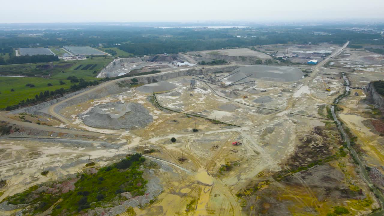 Aerial drone footage orbiting around a large limestone gray and yellow colored quarry or a mine where converyor belts, minging equipment and machinery is visible on cloudy summer. Gravel mountains