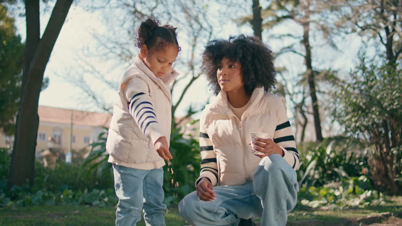 niño lindo lanzando migas a los pájaros de pie en el parque verde con la madre cariñosa.