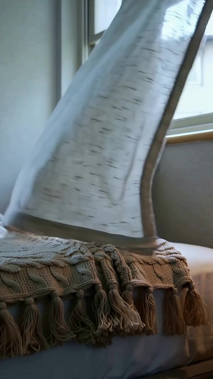 Video verticale: Una tenda che ondeggia fluttua sopra il letto in camera da letto da una finestra aperta, rivelando un plaid.