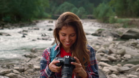 Hiker-standing-at-river-shore-with-photo-camera.-Happy-girl-using-camera