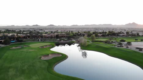 drone footage from a golf course near a residential neighborhood in arizona. high aerial shot of the greens, fairway, water harzard and clubhouse, with the arizona mountains in the background