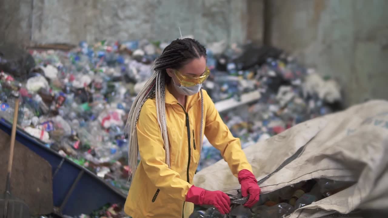 mujer voluntaria con gafas protectoras amarillas y transparentes clasificando botellas de plástico usadas en una moderna planta de reciclaje.