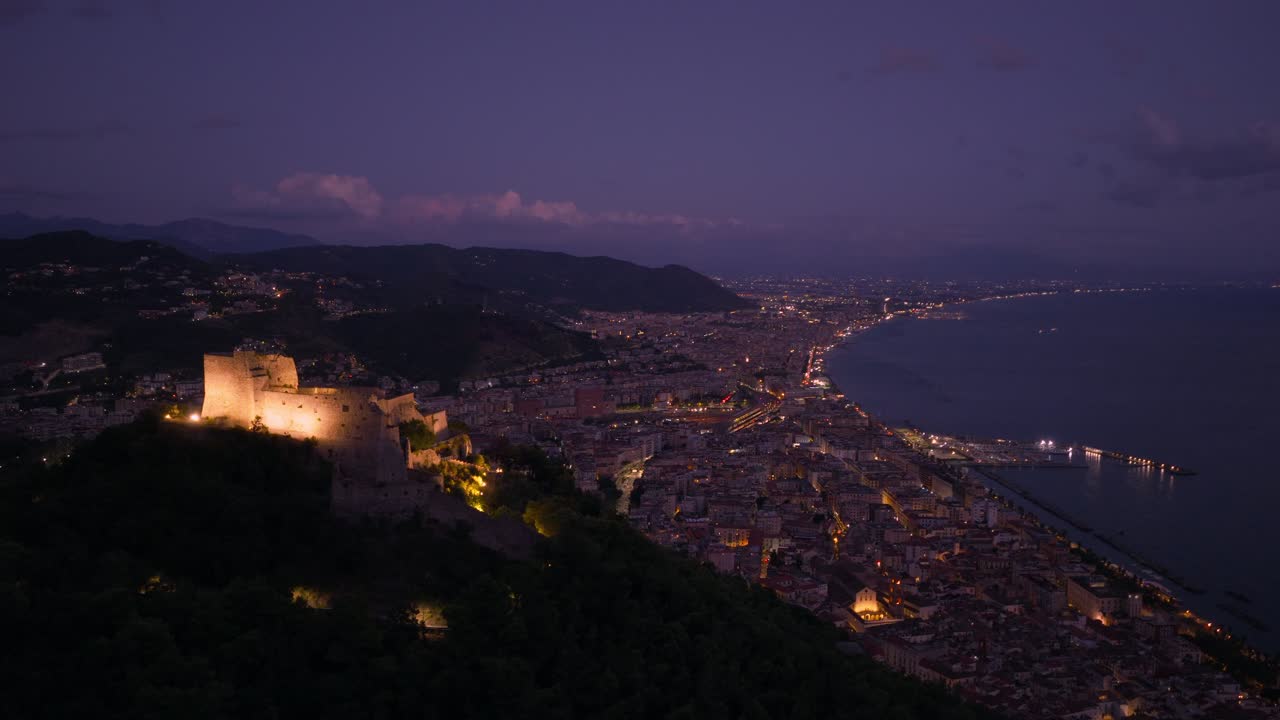 Mountaintop Medieval Fortress Of Arechi Castle At Night Overlooking The City Of Salerno In Italy. Aerial Drone Shot