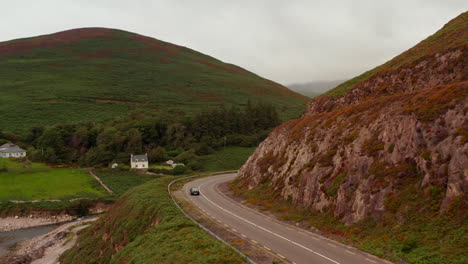 Tracking-of-car-passing-through-curves-around-steep-rock-slope.-Road-leading-in-countryside.-Ireland