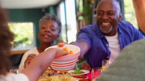 multi-generation family sitting around table at home enjoying meal together