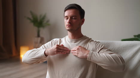 man meditating with hands on his chest in a calm indoor setting
