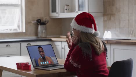 Caucasian-woman-wearing-santa-hat-on-laptop-video-call-during-christmas-at-home