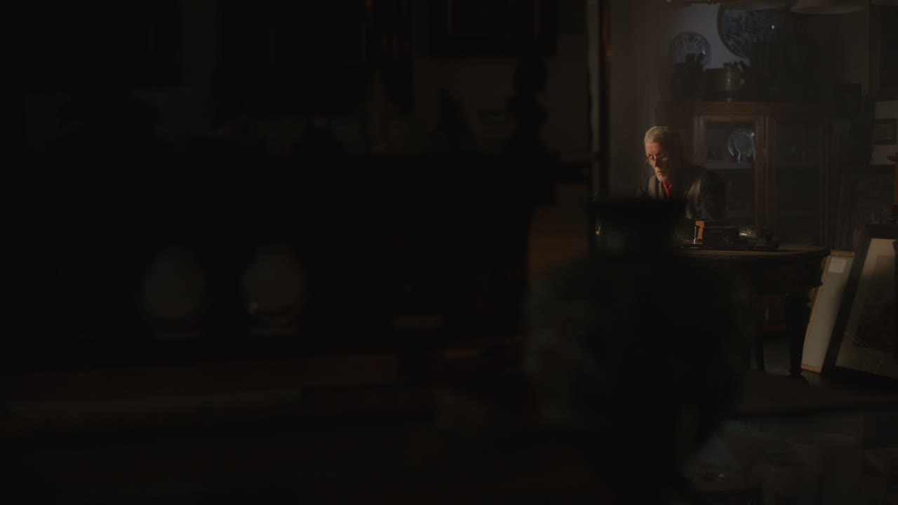 Older passionate man evaluates an old watch in his office at night