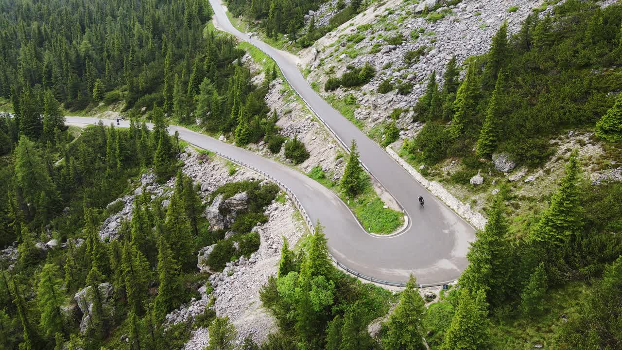 Black bikepacker rides downhill on Italian alpine road Passo Sella, static drone