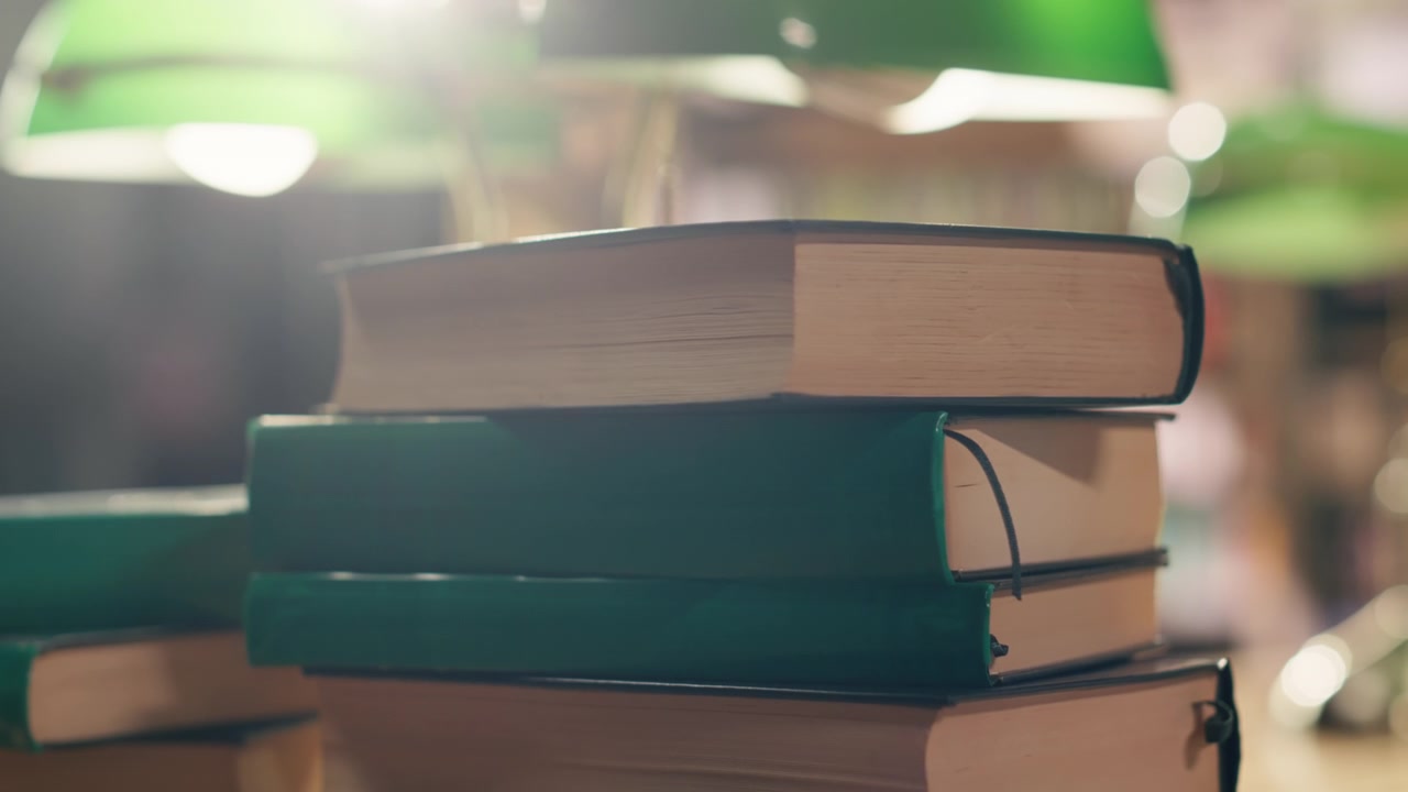 Stack of books on desk in quiet university library with warm lighting