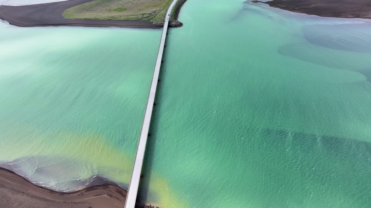 Drone video of vehicles driving over a land bridge crossing the Olfusa River in southern Iceland on a clear beautiful day in the land of fire and ice