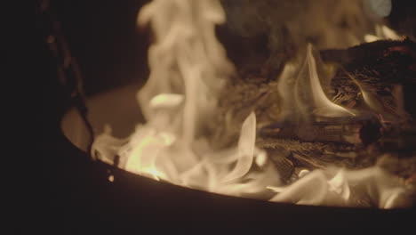 Slowmotion shot of a fire and flames burning away a newspaper in a fire pit creating sparks and smoke tilting upwards LOG