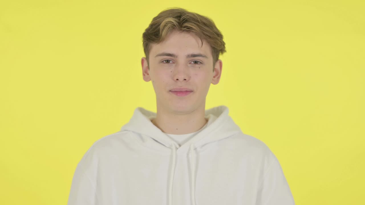 노란색 배경 에 "예"라는 표시 로 머리 를 흔들고 있는 젊은 남자