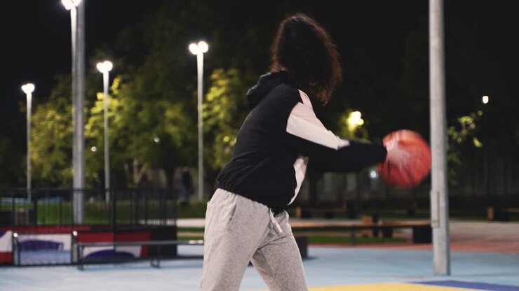 Concentrated Female Basketball Player Training With Ball On Outdoor Court At Night