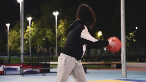 concentrated female basketball player training with ball on outdoor court at night