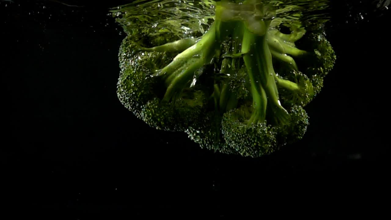 Falling of cabbage of broccoli in water. Slow motion. Black background