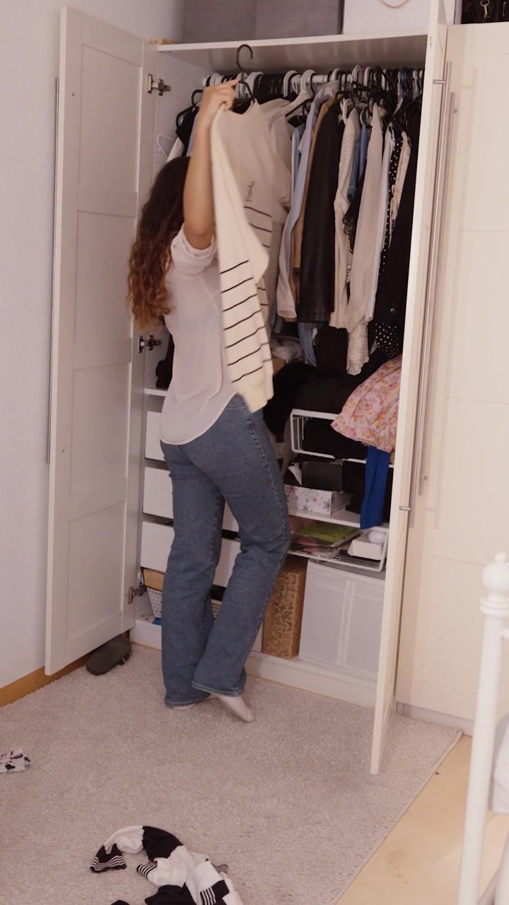 A woman searches through her wardrobe and throws clothes onto the floor while looking for an outfit.