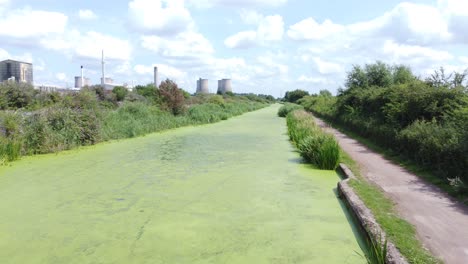 綠色藻類覆蓋的運河水道導向發電廠工業空中無人機視角低向前射擊