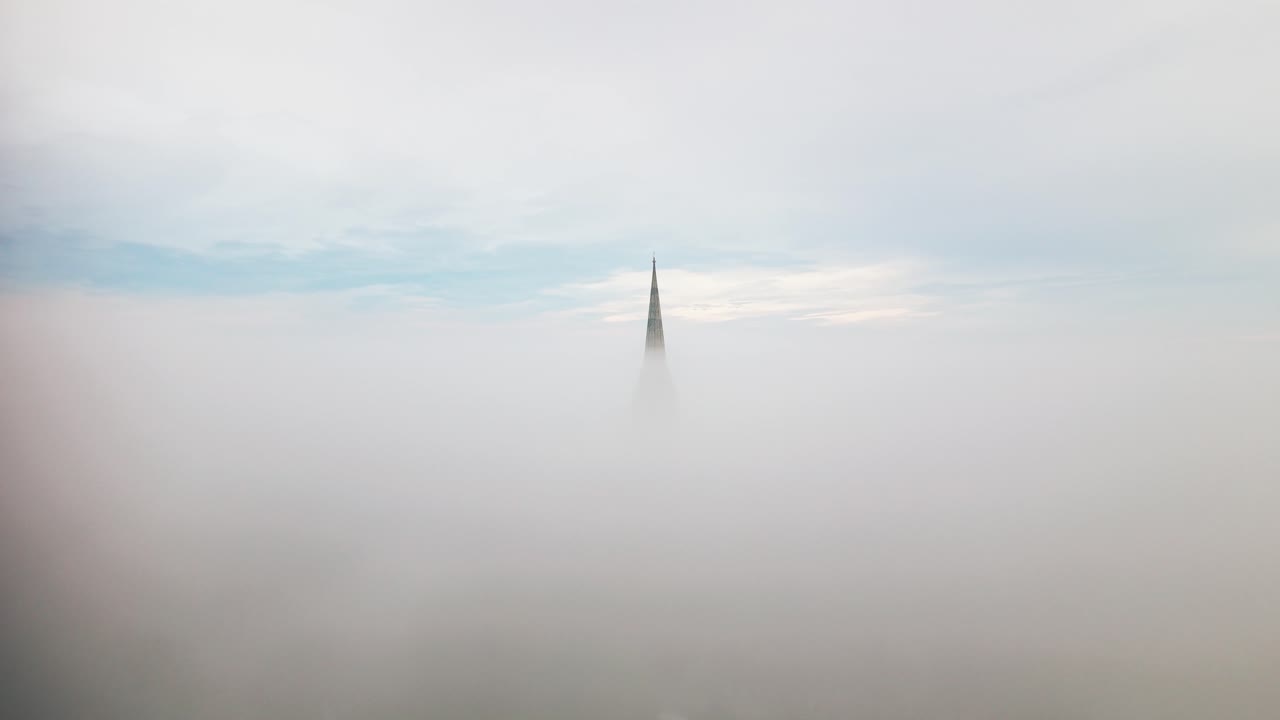 Droneoptagelse af Salisbury Katedrals spir, der rager op over tyk morgentåge og lave skyer over Salisbury, Wiltshire, England.
