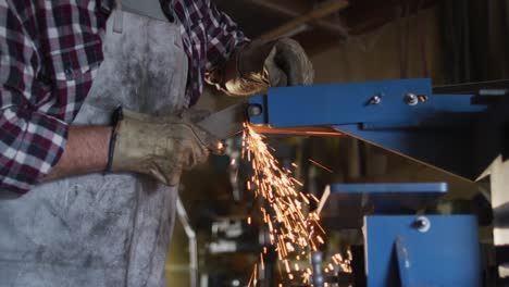 sección media de un hombre caucásico fabricante de cuchillos en un taller utilizando un molinillo angular