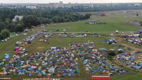 aerial view of multi-colored tents pitched in a field at a music festival with city in the background