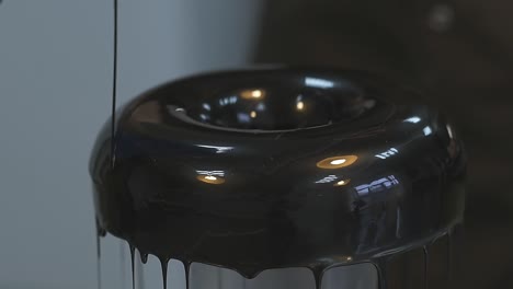 confectioner pours dark chocolate topping on doughnut