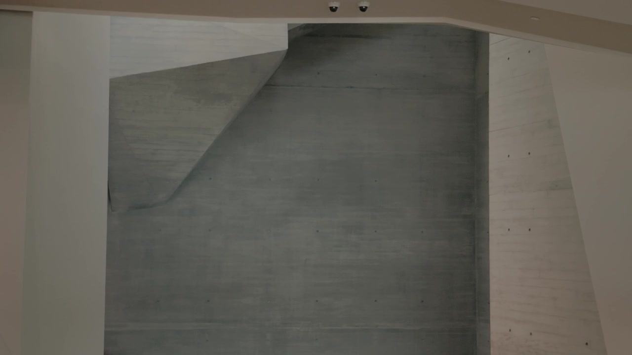 An upward pan from a high angle reveals concrete surfaces and an upper balcony.