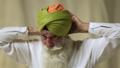 une photo en studio d'un homme sikh âgé avec une barbe liant du tissu pour un turban contre un fond plat prise en temps réel