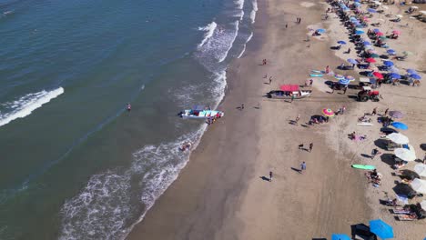 A-drone-flies-above-of-people-sun-tanning-on-the-beach-below-with-beach-umbrellas-and-lounge-chairs-in-Sayulita-Mexico