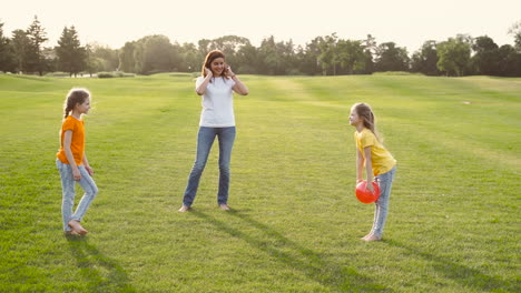 madre feliz y sus dos hijas pequeñas jugando con pelota en el prado
