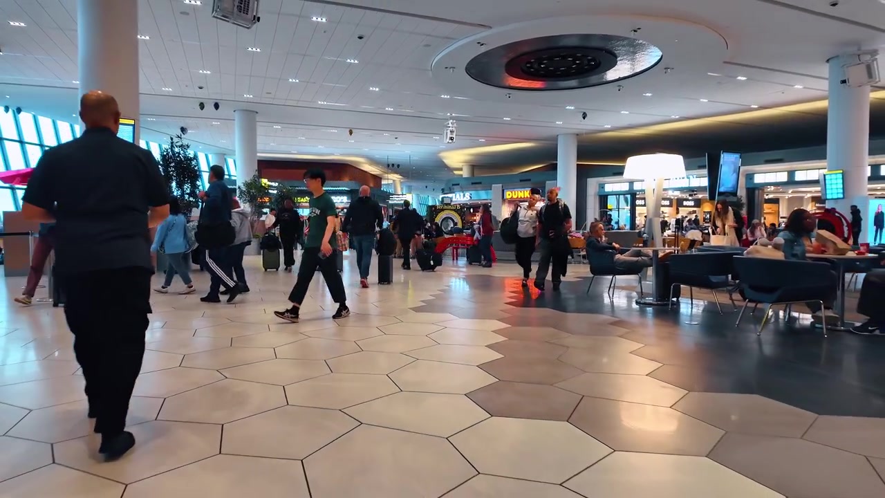 Chicago, USA, 27 maggio 2026: Viaggiatori con bagagli nell'area ristorazione del terminal aeroportuale. I passeggeri trascinano valigie a rotelle oltre i banconi dei ristoranti, i posti a sedere e i cartelli all'interno di un atrio.