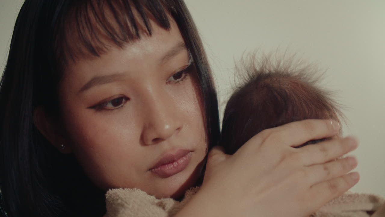Mother Gently Holding Her Crying Baby in a Tender Moment, asiatic young mom and her newborn