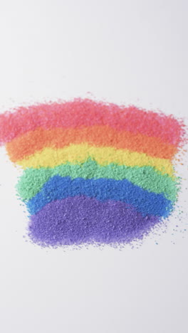 vertical video of close up of rainbow coloured sand grains and copy space on white background