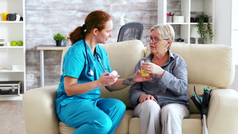 Female-doctor-sitting-on-sofa-with-senior-woman-in-nursing-home-giving-her-daily-pills