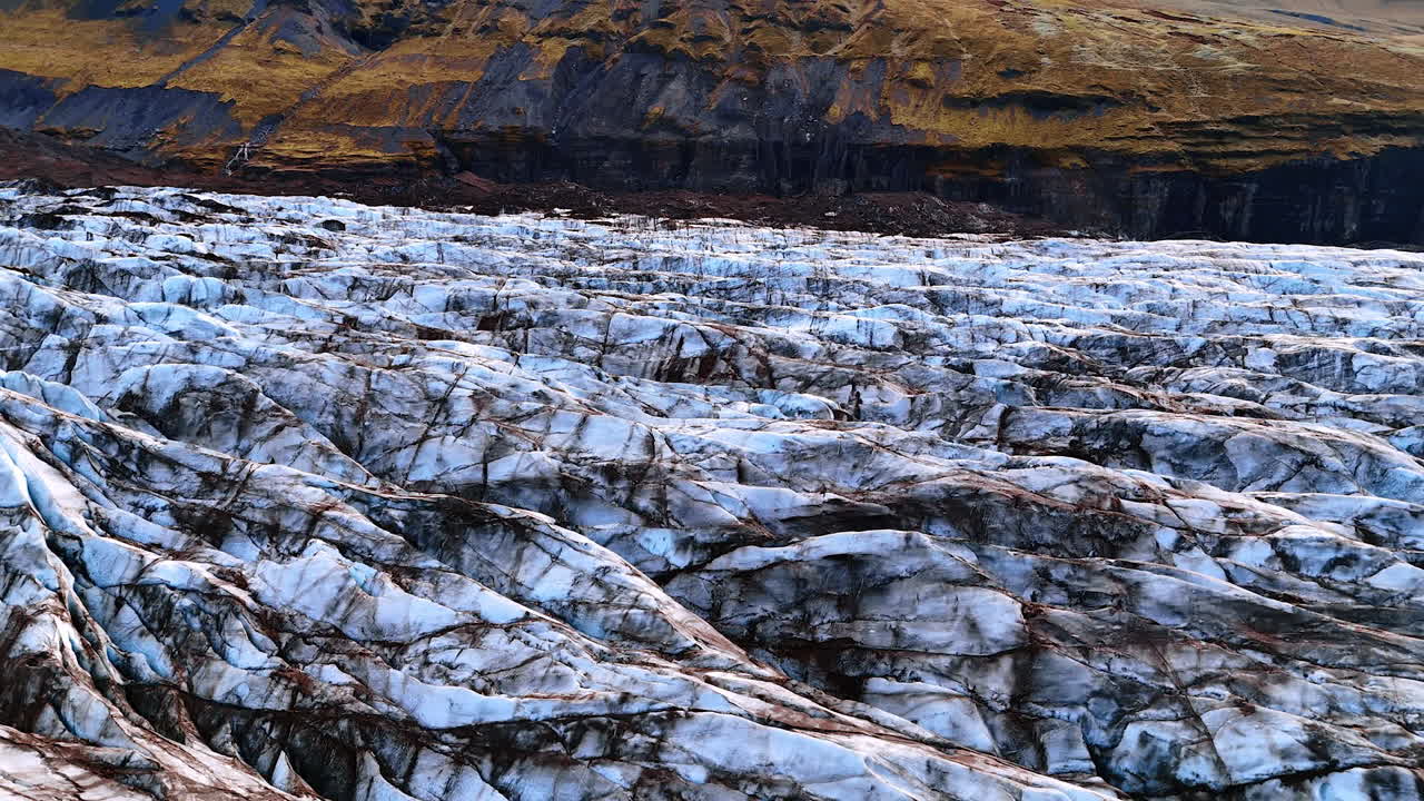 Ranges of ice hills of the old glacier of marble coloring. Bare rocks at backdrop. Landscape of Iceland from top view.
